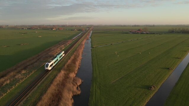 Stavoren, Netherlands - 10 May 2023: Aerial view of train driving through countryside near river, Netherlands