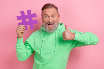 Photo of positive confident guy dressed green hoodie showing thumb up hash tag card isolated pink...