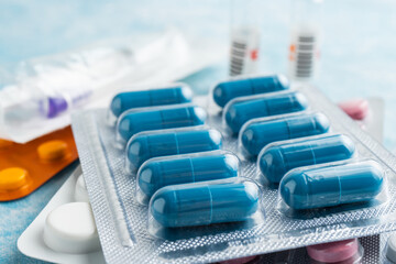 Pile of various capsules, pills and tablets in a blister pack on blue background, healthcare and...