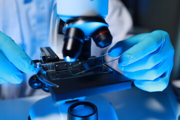 A talented scientist sits in his lab while using a microscope to look for microscopic organisms in...