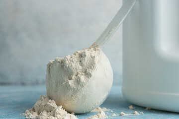 Whey protein powder in measuring spoon on a blue background