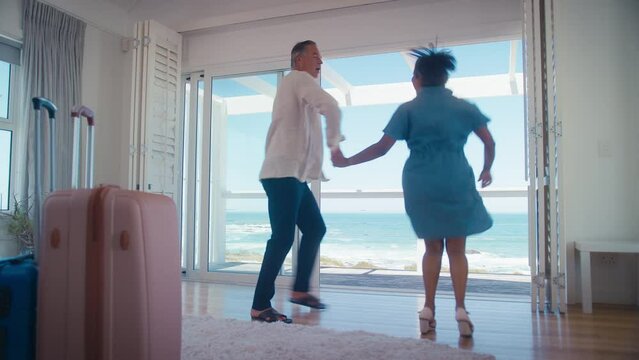 Low angle shot of mature couple with luggage arriving for holiday in beach front property overlooking ocean dancing together - shot in real time