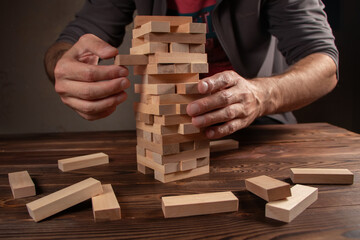 Hand of engineer playing a blocks wood tower game on blueprint or architectural project