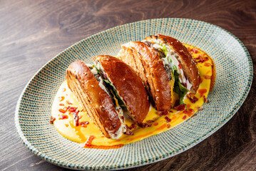 A gourmet burger with melted cheese, bacon, onions, lettuce, and sauce on a sesame seed bun in cheese sauce