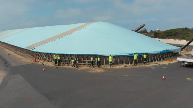 Geraldton, Australia - 10 November 2021: Aerial view of workers closing open bulkhead grain storage with tarp, Australia