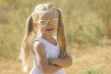 A blonde girl in a white dress on the street in sunglasses looks into the frame