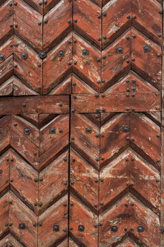 wooden brown painted door composed of zigzag planks placed. it is a lining that is nailed with metal rivets or nails