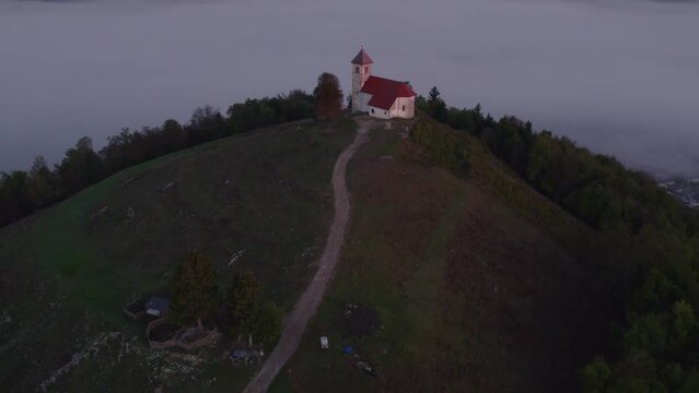 Aerial view of St. Anne's Church (Cerkev sv. Ane) on top of a mountain with low fog, Jezero, Slovenia