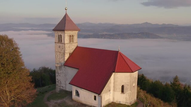 Aerial view of St. Anne's Church (Cerkev sv. Ane) on top of a mountain with low fog, Jezero, Slovenia