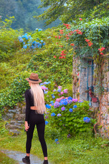 A stylish beautiful blonde woman walking around the beautiful garden of an old stone house