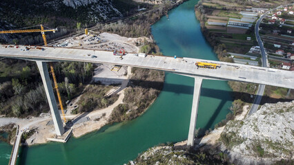 Construction of a high bridge over the river, aerial drone view. Workers and machines on...