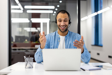 Friendly businessman with headset smiling at laptop screen