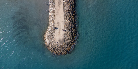 Aerial view of a breakwater stretching into the sea. Tranquility of ocean waves meeting the structure. Ideal for backgrounds or travel concepts - obrazy, fototapety, plakaty