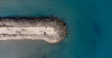Top view of a breakwater with large boulders jutting into the sea. Surrounded by a calm sea. Ideal...