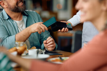 Close up of father using smartphone while paying to waitress in restaurant.