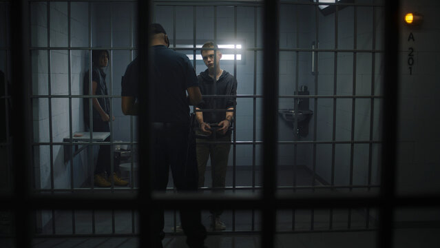 Warden brings young prisoner in jail cell and takes off his handcuffs. Multi ethnic teenagers serve imprisonment term in correctional facility or detention center. Guilty inmates in prison cells.