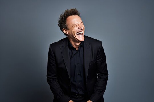 Portrait of a laughing man in a black suit on a gray background.