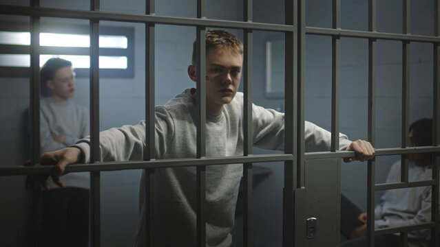 Portrait of diverse teenage prisoners behind metal bars in prison cell looking at camera. Multiethnic young inmates serve imprisonment terms in jail. Juvenile detention center or correctional facility