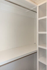 Interior white solid wood closet with wood shelves and a clothing bar