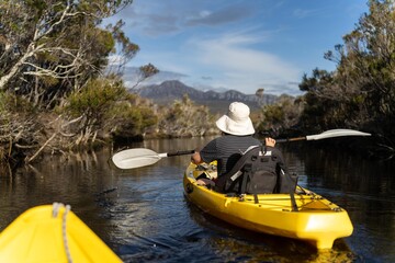 kayaking up  a river in a canoe with mountains in a wilderness in a national park with native plants and trees in a rainforest in Australia. with rivers and exploring  in australia