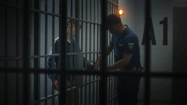 Warden takes off handcuffs from young prisoner. Teenager serves imprisonment term in correctional facility or detention center. Young inmate in prison cell. Justice system. View through metal bars.
