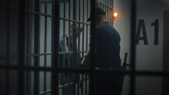 Warden takes off handcuffs from young prisoner. Teenager serves imprisonment term in correctional facility or detention center. Young inmate in prison cell. Justice system. View through metal bars.