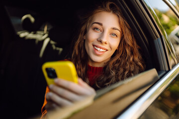 Happy  woman uses a smartphone while sitting in the back seat of a car. Young woman checks mail,...