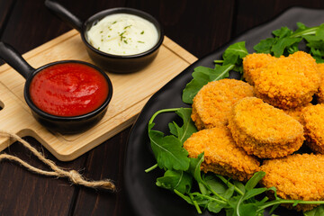Close-up Nuggets, Dipping Sauce and rocket leaves on a dark background, space for text, selective focus. Fast food. Protein Meals concept.