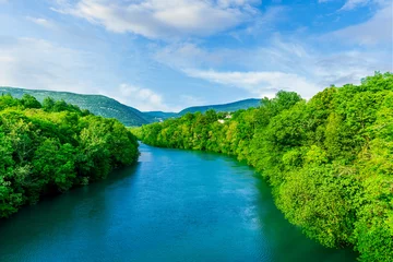 Foto auf Leinwand beautiful landscape of spring or summer sunset river with blue water and green hills on sides and mountains with amazing cloude sky on background © Yaroslav
