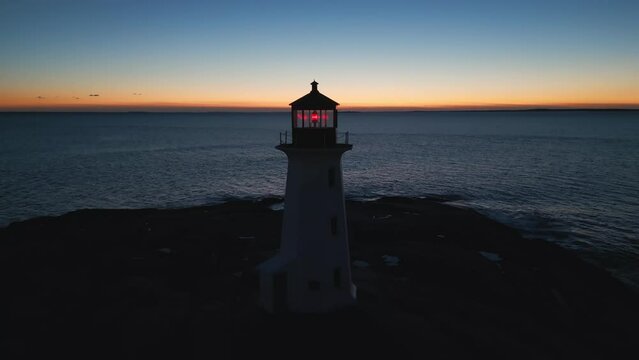 Cinematic drone shot Coastal lighthouse, Peggy's Cove Lighthouse against sunset sky at dusk, Atlantic Coast Lighthouse Halifax Nova Scotia Canada. The light comes from a first order Fresnel lens. 