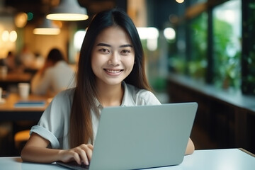 Young Asian happy business woman using laptop computer while sitting in office. Looking at camera and smiling