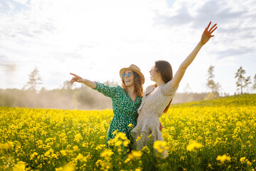 Two young women in a beautiful field with yellow flowers. They jump and have fun. Friendship Day