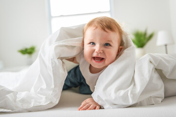 Fototapeta premium Baby boy in white sunny bedroom. one years child relaxing in bed.