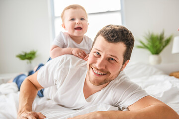 Obraz na płótnie Canvas bearded father holding baby boy on bed, fatherhood and love