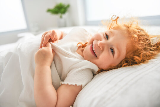 Redhead girl on the bed rests and plays. Cute little girl