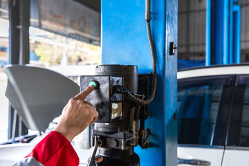 Car mechanic pushing button to open hydraulic machine in auto repair shop