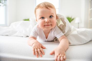 Baby boy in white sunny bedroom. one years child relaxing in bed.