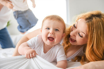 Mother and baby boy on bed, having great moment together on white bedroom