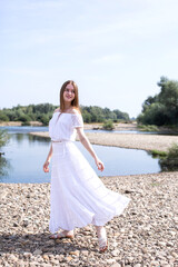 Fototapeta na wymiar Woman in white dress. Relaxation. Portrait of a woman. Creative. Cheerful woman dancing in nature. River and stones