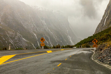 Water from torrential rain and snow-melt rushes down steep rockfaces toward a hairpin turn on State Highway 94, in Fiordland, New Zealand, the road to Milford Sound - obrazy, fototapety, plakaty