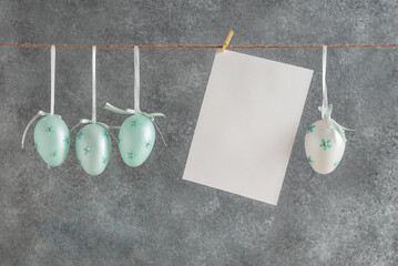 Turquoise Easter eggs and a blank white card hanging on a rope, gray grunge background. - 758904822