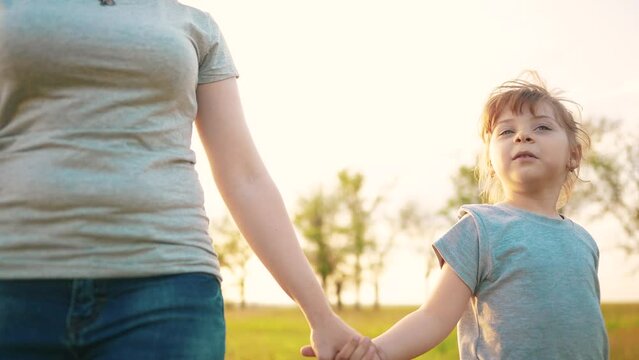 mother daughter walking in the park. happy family kid dream concept. close-up daughter holding her mother hand walking along sunlight the road in the park in nature. mom daughter outdoors in the park