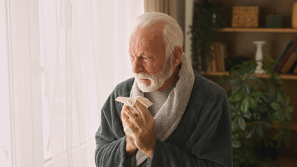 Senior man blowing his nose indoors