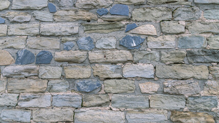 The background of the masonry. An ancient wall made of multicolored stones. The raw stones are stacked to form a wall.
