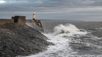 Rough seas and waves crashing into a sea wall and lighthouse (Porthcawl, South Wales, UK) on a cloudy, winters day