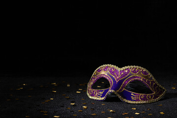 Masquerade mask with confetties on black background.