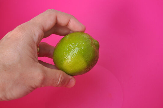 mão segurando limão em fundo rosa 
