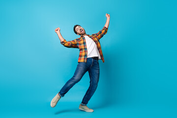 Obraz premium Full body photo of attractive young man dancing raise fists celebrate wear trendy plaid clothes isolated on blue color background