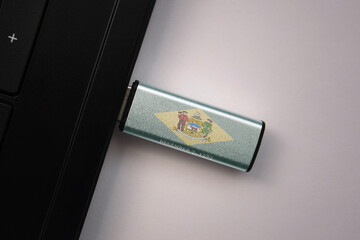 usb flash drive in notebook computer with the national flag of delaware state on gray background.