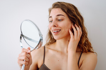 Portrait of a young girl with problem skin looks in the mirror. Pimples on the face. Facial skin...